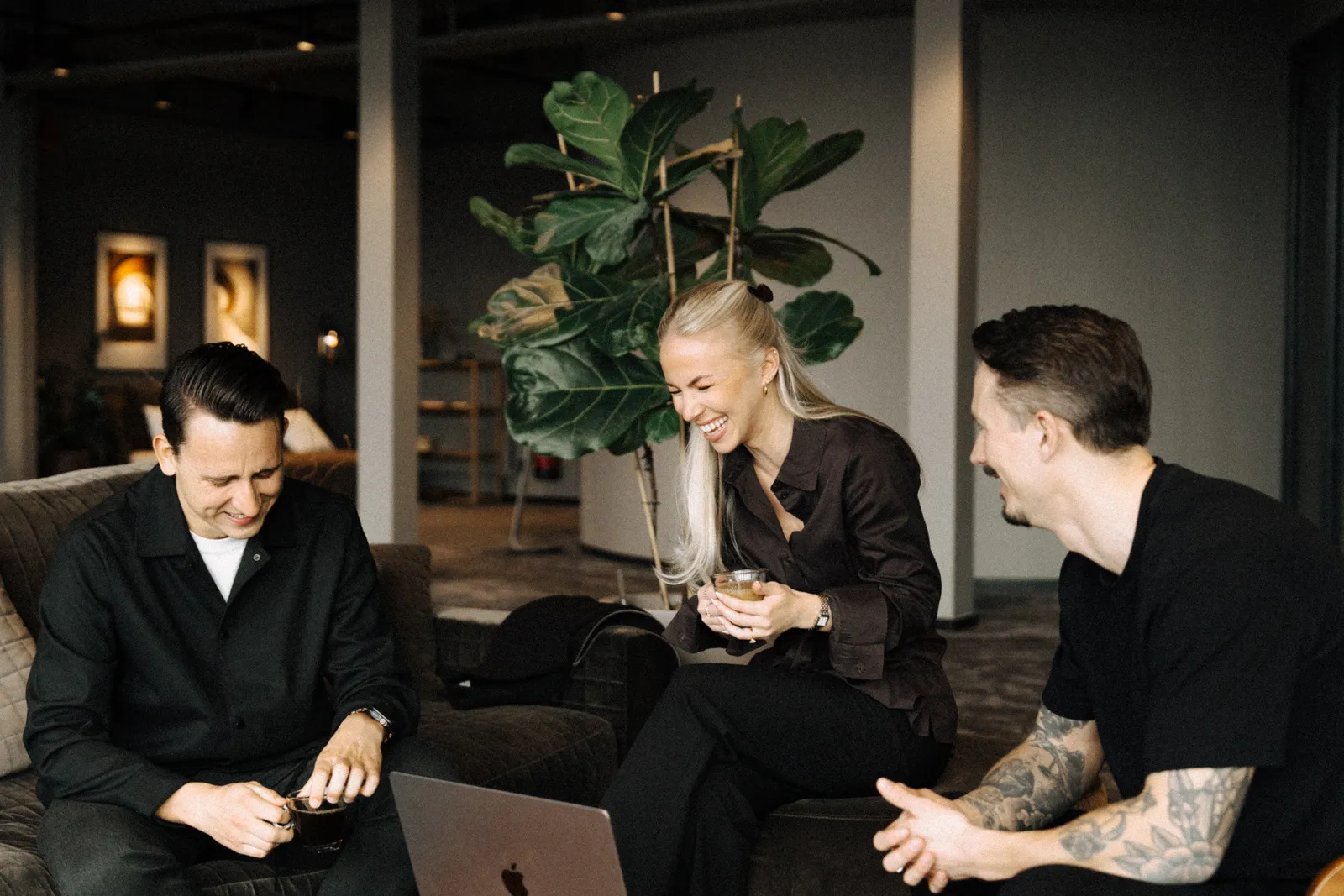 Tre från Maraton skrattar tillsammans i soffgruppen med kaffe och en laptop